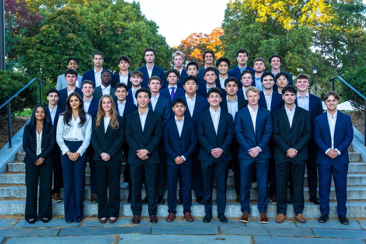 The 2026 Purple Group cohort in suits on stone steps on the Amherst campus in October